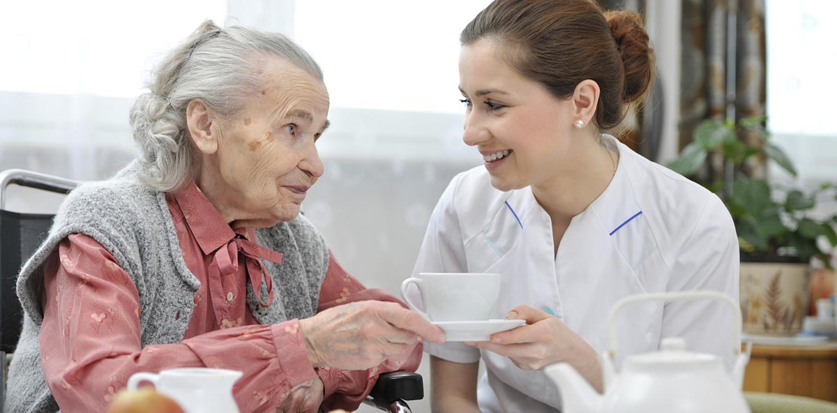 caregiver helping elderly client handing a cup to drink